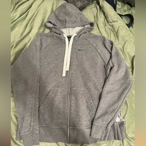 Grey Nike zip up. Has a hood and strings. The sides of the jacket flip up.